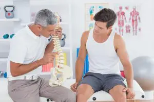 A chiropractor holding a model of a spine and talking about herniated discs to a patient