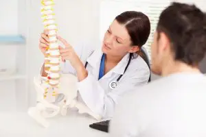 A chiropractor showing a model of a spine to a patient explaining the conditions treated in Fort Wayne & New Haven