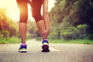 A zoomed-in shot focusing an injured ankle of a female jogger and her other hand holding it