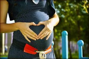 pregnant woman holding her belly forming a heart with her hands after experiencing chiropractic prenatal care in Fort Wayne