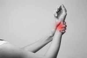 A wrist in pain held by another hand with a red mark as the pain indicator and the image in grayscale