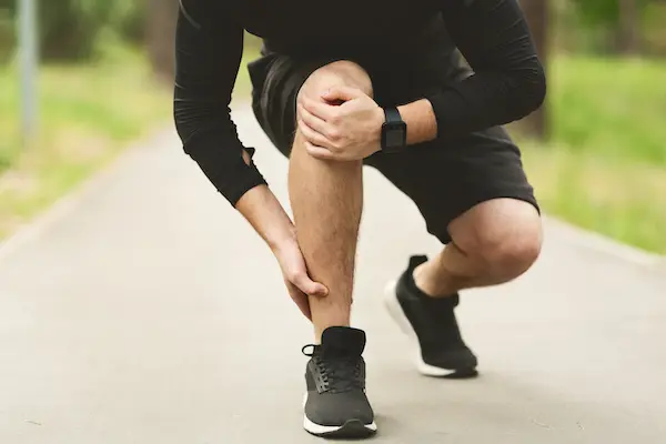 male runner holding his knee and ankle due too joint pain