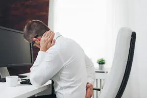 man holding his back due to pain sitting in chair