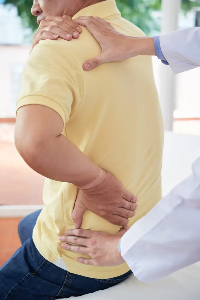 doctor examining male patient upper back due to pain