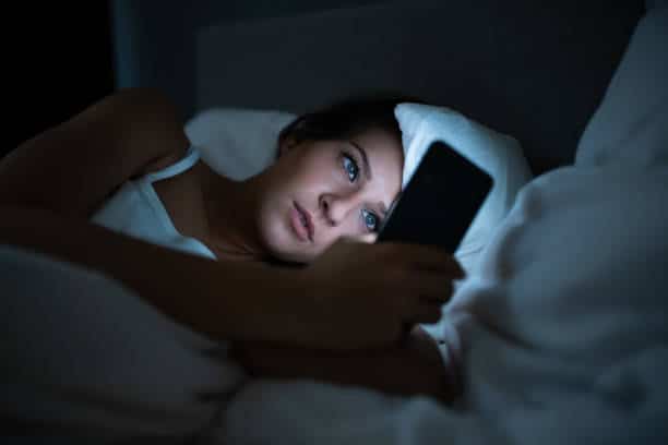 Woman in bed playing her phone at night 