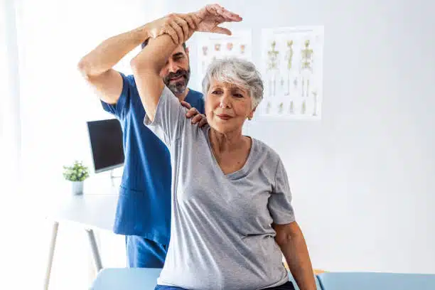 Male doctor chiropractor or fixing woman's shoulder with hands movements during visit in chiropractic clinic.